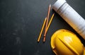 Yellow hard hat, rolled blueprints, pencils rest on dark surface. Elements suggest construction project planning phase. Royalty Free Stock Photo