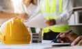 Yellow hard hat on workbench with Engineer teams meeting working together wear worker helmets hardhat on construction site. Asian Royalty Free Stock Photo