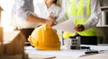 Yellow hard hat on workbench with Engineer teams meeting working together wear worker helmets hardhat on construction site. Asian Royalty Free Stock Photo