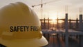 Yellow hardhat with the text Safety First sits in the foreground with a blurred construction site featuring a crane and Royalty Free Stock Photo