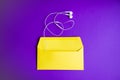 Yellow headphones on envelopment on purple background.