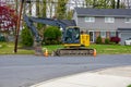 Yellow heavy equipment excavator parked on the side of a residential street in front of a house with orange warning cones Royalty Free Stock Photo