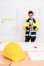 Yellow Helmet On Table With Contractor Using Phone In Office