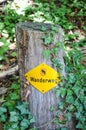 Yellow hiking trail mark on a wooden stump in the forest. Sign TRANSLATION: Wanderweg - trail, hiking path in German. Tourist