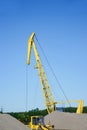 Yellow hoisting crane on a background of clear blue sky. Construction machinery and a mountain of rubble