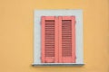 yellow house facade and window with closed red shutters, exfoliated paint