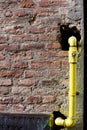 Yellow hydraulic hose coming out of a brown brick wall. Royalty Free Stock Photo