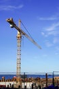 Yellow industrial crane with boom towards blue sky at summer time. Blue sea on the back