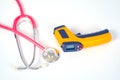 Yellow Infrared thermometer gun used to measure temperature with stethtoscope on white background