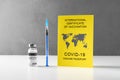 Yellow International Certificate of Vaccination, syringe, vial with vaccine on gray background