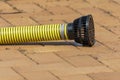 Yellow irrigation suction hose with a black filter lying on brown bricks