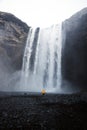 Yellow jacket person tourist at famous wide Skogafoss cliff waterfall Skoga river near Skogar South Iceland Europe Royalty Free Stock Photo