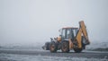 Yellow construction tractor is driving on the foggy road during the cold autumn