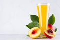 Yellow juice in glass and juicy ripe red nectarines with green leaves, slice, seed on soft light white wood board, closeup. Royalty Free Stock Photo