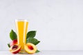 Yellow juice in glass and juicy ripe red nectarines with green leaves, slice, seed on soft light white wood board. Royalty Free Stock Photo