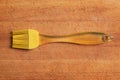 A yellow kitchen silicone brush sits on a worn cutting board