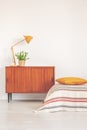 Yellow lamp and plant in pot on vintage cabinet in elegant bedroom interior, real photo with copy space on the empty wall Royalty Free Stock Photo