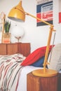 Yellow lamp on wooden stool next to bed with red pillow in teenager`s bedroom interior. Real photo