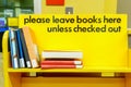 Yellow library book cart with sign, and books stacked on a shelf to be put away