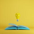 Yellow light bulb floating from opened blue book on yellow background.