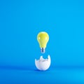 Yellow light bulb floating from white eggshell on blue background. Royalty Free Stock Photo