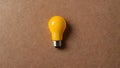 A yellow light bulb resting on a warm-toned brown surface.
