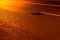 Yellow light on night road pavement with sewer manhole