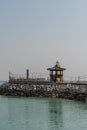 Yellow lighthouse behind oriental gazebo on seaside pier with gray sky in background