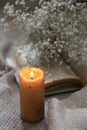 a yellow lit candle in front of a bunch of small white blossoms on an open book on a cloth