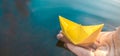 Yellow lonely floating paper boat in hand. Colorful sailing ship in big blue spring puddle, river water.Warm wet rainy Royalty Free Stock Photo