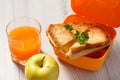 Yellow lunch box with toasted slices of bread, cheese and green parsley, green apple and glass of orange juice on wooden desk Royalty Free Stock Photo