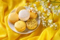 Yellow macaroons on a white elegant saucer against bright yellow draped tablecloth. Sweet breakfast with delicious almond meringue