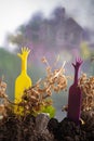 Yellow, magenta plastic hands stick out of the ground with dry brown flower stems near foil shining toy rocket. Happy family,