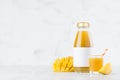 Yellow mango juice in glass bottle mock up with blank label, straw, wine glass, fruit slice on white wood table in light interior. Royalty Free Stock Photo
