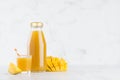 Yellow mango juice in glass bottle mock up with straw, wine glass, fruit slice on white wood table in light interior, template. Royalty Free Stock Photo