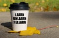 On a yellow maple leaf there is a cup of coffee on which is written - learn unlearn relearn Royalty Free Stock Photo