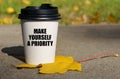 On a yellow maple leaf there is a cup of coffee on which is written - Make yourself a priority Royalty Free Stock Photo