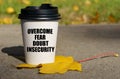 On a yellow maple leaf there is a cup of coffee on which is written - overcome fear, doubt, insecurity Royalty Free Stock Photo