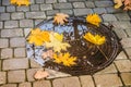 Yellow maple leaves on the manhole cover after the rain. Manhole cover in water and leaves in autumn. A manhole cover in autumn Royalty Free Stock Photo