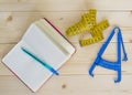 Yellow measuring tape, blue kaliper and notebook with pen on wooden table