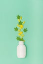 Yellow medical cbd capsules and green small toy cannabis leaves fly out of the white plastic bottle on green background. Medical