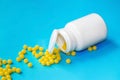 Yellow medical pills spilled out of white bottle and tablets on blue background with copy space Royalty Free Stock Photo