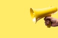 Yellow megaphone on a yellow background in a man`s hand. Symbol of false information, rumors, fakes. Election debates, advertisin