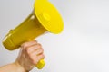 Yellow megaphone in a man`s hand on a white background. Minimalism. News, rumors, gossip, democracy, press, elections, debates.