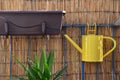 Yellow metal watering can hang on balcony railing, bamboo fence in background Royalty Free Stock Photo