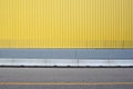 Yellow metallic cladding wall with a gray concrete barrier. Sidewalk and asphalt road in front. Royalty Free Stock Photo