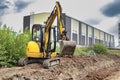 Yellow mini excavator at the construction site on the edge of a pit against a cloudy blue sky. Compact construction equipment for Royalty Free Stock Photo