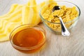 Yellow napkin, bowls with honey, spoon in bowl with corn flakes on wooden table Royalty Free Stock Photo