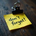 Yellow note with dont forget message clipped to dark wood table. Reminders aid daily task planning and personal organization. Royalty Free Stock Photo