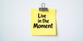 Yellow Note with Live in the Moment Message on White Surface for Daily Motivation and Mindfulness Royalty Free Stock Photo